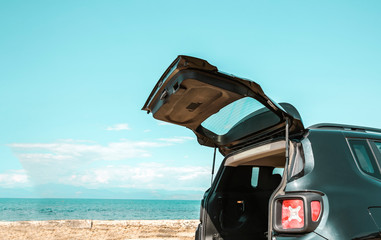 Black large car with an open luggage carrier parked on the beach. Sea landscape and free space for your product or text. Summer and sunny warm day. Copy space.