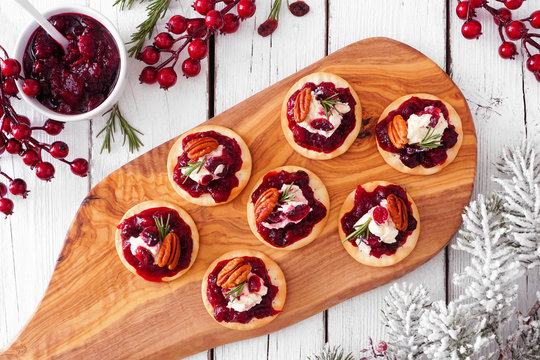 Platter of holiday appetizers with cranberries, goat cheese and pecans. Top view serving scene on a white wood background