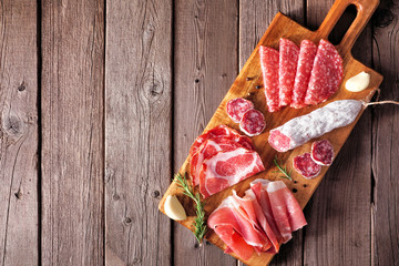 Italian antipasto meat platter with sausage, prosciutto, ham and salami. Top view on a serving board against a wood background.