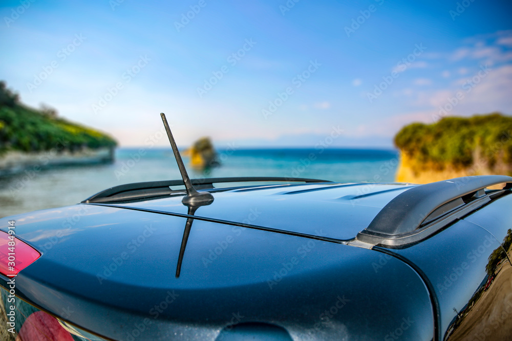 Poster Young woman in a straw hat and sunglasses. Dark soul car on the beach. View of beautiful sea and blue sky. Place for your text or product. A beautiful summer day. Car trip and sightseeing of the coast