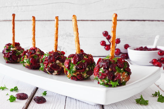 Christmas cheese ball appetizers with cranberries, pecans and herbs. Close up on a serving plate with a white wood background.