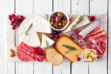 Serving platter of assorted meats, cheeses and appetizers. Top view on a white wood background.