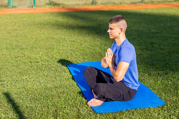 Young man wearing athletic wear sitting in the park exercising yoga