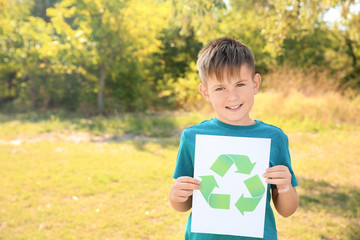Boy holding paper sheet with sign of recycling outdoors