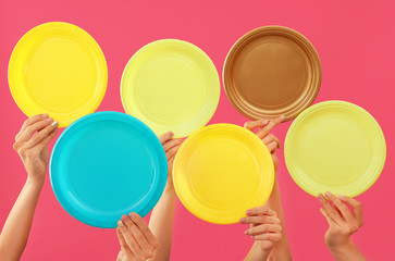 Many hands with empty plates on color background
