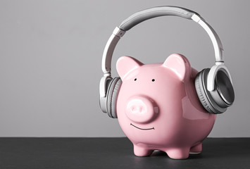 Piggy bank with headphones on grey background