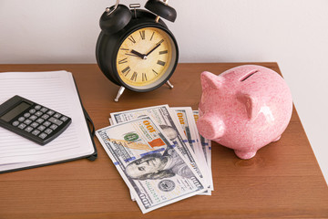 Piggy bank with alarm clock and money on table