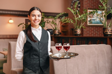 Young waitress with glasses of wine in restaurant