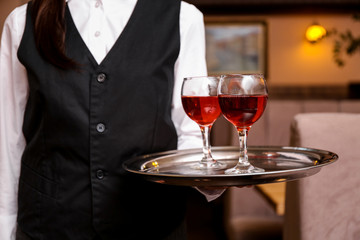 Young waitress with glasses of wine in restaurant, closeup