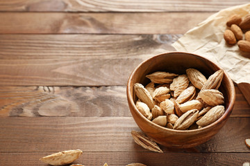 Bowl with tasty almonds on wooden table