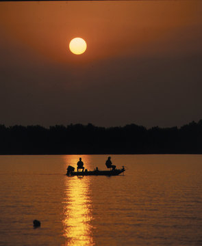 silohette of fishermen in boat on lake at sunset