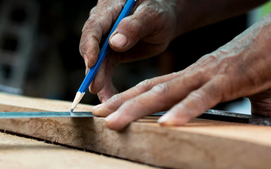 Close-up of a carpenter's hand, using a ruler and a pencil to make wood.