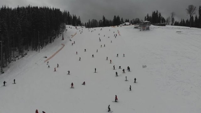 Aerial photography in the mountains of a winter resort. Ski slopes on the mountain slopes. Winter landscape of snow-capped peaks with dense pine forest.
