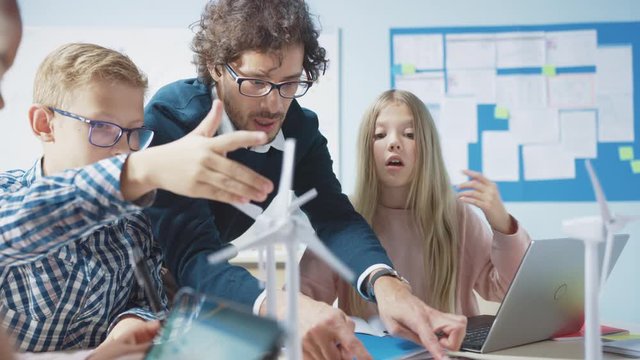 Elementary School Classroom: Enthusiastic Teacher Holding Tablet Computer Explains to a Brilliant Young Children How Wind Turbines Work