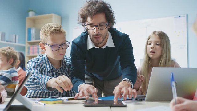 Elementary School Classroom: Enthusiastic Teacher Holding Tablet Computer Explains Lesson to Brilliant Young Children. Kids Learning Programming Languages, Internet Safety and Software Design