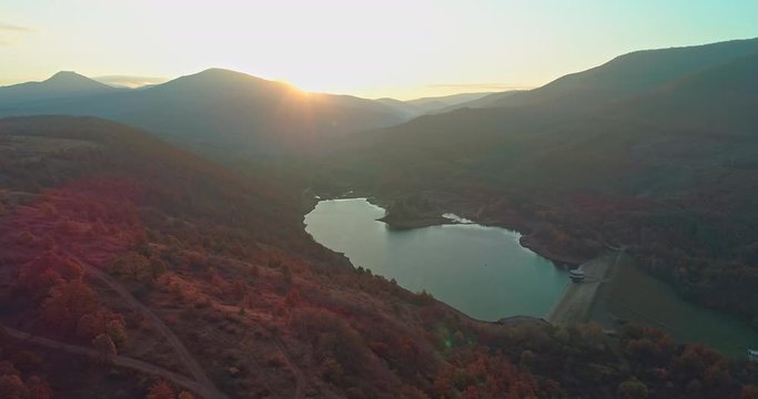 Levee drone aerial at sunrise with hills and mountains in Hungary, Hasznos. Sun rises behind the hills, reflections on the water.