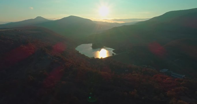 Levee drone aerial at sunrise with hills and mountains in Hungary, Hasznos. Sun rises behind the hills, reflections on the water.