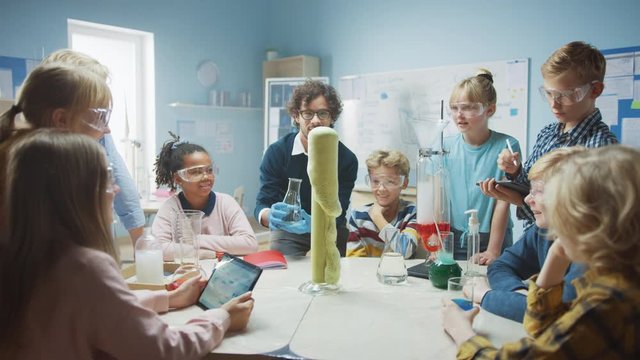 Elementary School Science / Chemistry Classroom: Enthusiastic Teacher Shows Funny Chemical Reaction Experiment to Group of Children. Mixing Chemicals in Beaker so they Shoot Foam (Elephant Toothpaste)