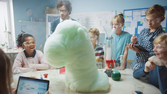 Elementary School Science / Chemistry Classroom: Enthusiastic Teacher Shows Funny Chemical Reaction Experiment to Group of Children. Mixing Chemicals in Beaker so they Shoot Foam (Elephant Toothpaste)