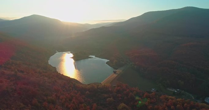 Levee drone aerial at sunrise with hills and mountains in Hungary, Hasznos. Sun rises behind the hills, reflections on the water.