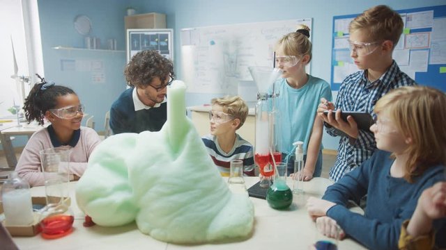 Elementary School Science / Chemistry Classroom: Enthusiastic Teacher Shows Funny Chemical Reaction Experiment to Group of Children. Mixing Chemicals in Beaker so they Shoot Foam (Elephant Toothpaste)
