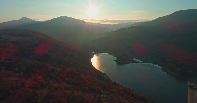 Levee drone aerial at sunrise with hills and mountains in Hungary, Hasznos. Sun rises behind the hills, reflections on the water.