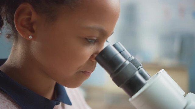 Portrait of Smart Little Schoolgirl Looking Under the Microscope. In Elementary School Classroom Cute Girl Uses Microscope. STEM (science, technology, engineering and mathematics) Education Program
