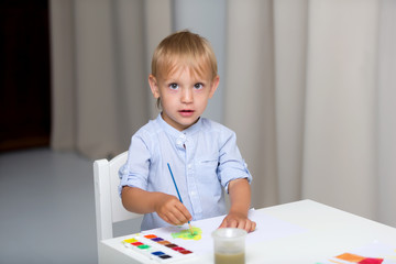 Cute little boy paints with watercolors while sitting at the tab