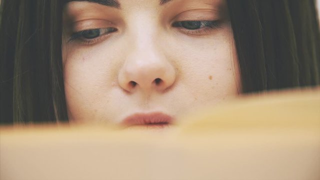 Cropped face of nquisitive young female reading a book, moving eyes back and forth along the page.