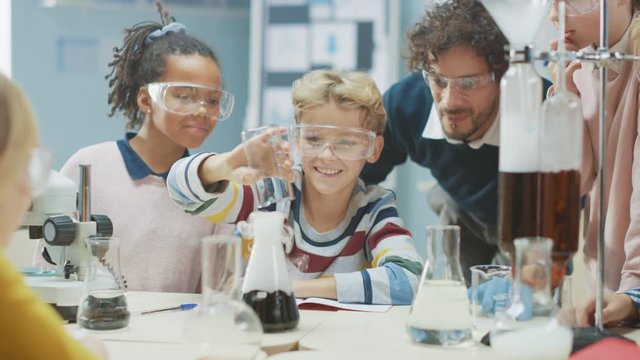 Elementary School Science Classroom: Enthusiastic Teacher Explains Chemistry to Diverse Group of Children, Little Boy Mixes Chemicals in Beakers. Children Learn with Interest