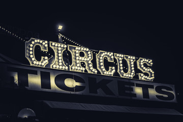 Spooky old dimly lit circus sign with light bulbs in the dark over a ticket stand in black and...