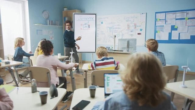Elementary School Physics Teacher Uses Interactive Digital Whiteboard to Show to a Classroom full of Smart Diverse Children how Generator Works. Science Class with Curious Kids Listening Attentively