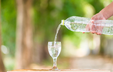 Water splash in glass Select focus blurred background.Drink water pouring in to glass over sunlight and natural green background.Nature conservation concept.