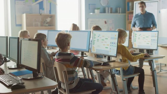 Elementary School Science Classroom: Teacher Educates Smart Little Schoolchildren who Work on Personal Computers, Learn Programming Language for Software Coding. Boy Raises Hand with a Question