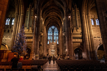 LIVERPOOL, ENGLAND, DECEMBER 27, 2018: People walking along the entrance hall of the Church of England Anglican Cathedral of the Diocese of Liverpool with a christmas tree aside during holidays. - obrazy, fototapety, plakaty