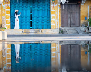 Vietnamese Woman in Traditional White Garment Standing in Front of Turquoise Door