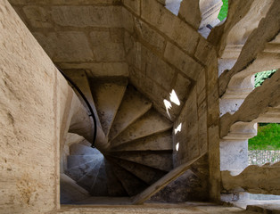 Top view of a spiral staircase made of stone. Between the balusters a green lawn is visible. Below...