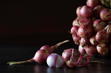 Bunch of shallot and some shallots fall off and peeled on dark wooden background which has dim light