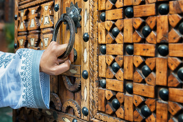 A hand holding a door handle of a traditional, wooden, moroccan door.