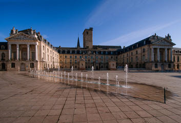 Fototapeta premium Pałac Książąt Burgundii w godzinach porannych. Niebo jest niebieskie. Miasto Dijon. Francja. Na pierwszym planie teren pokryty kamiennymi płytami oraz fontanna.