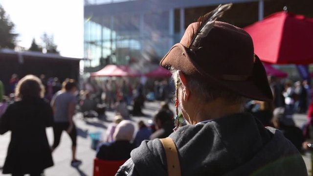 An elderly male activist in old fashioned mountaineers hat with selective focus is seen from the back listening to speeches at environmental rally