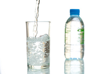 Drink water is poured into a glass. Close up pouring purified fresh drink water from the bottle on table and a fresh drinking water bottle on white background.