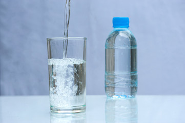 Drink water is poured into a glass. Close up pouring purified fresh drink water from the bottle on table and a fresh drinking water bottle on white background.