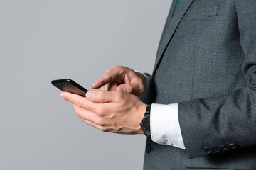 Businessman is writing sms on his mobile phone on gray background.