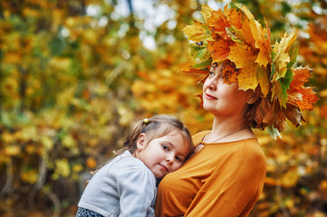 Portrait of a little girl and mother in the autumn Park, a girl with a wreath of maple leaves .