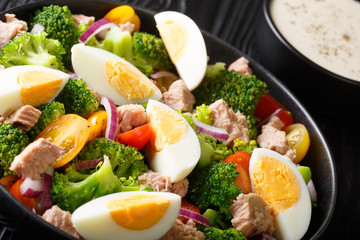 Breakfast salad with tuna, broccoli, tomatoes, onions and eggs and yogurt dressing closeup in a plate. horizontal
