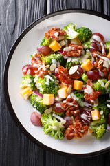 Broccoli salad with cheddar cheese, grapes, bacon, almonds and onions close-up in a plate. Vertical top view