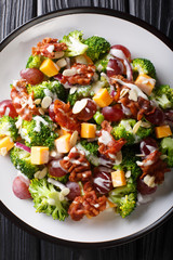 Tasty broccoli salad with cheddar cheese, grapes, bacon and onions close-up in a plate. Vertical top view