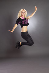 Fototapeta na wymiar Hübsches, junges, blondes Model Lisa Menig tanzt vor grauem Hintergrund und springt. Fitness, tanz und Springen im Studio