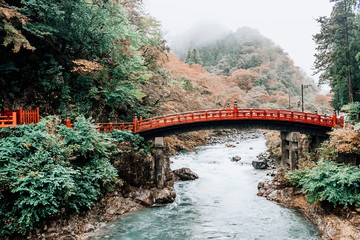 Red Shinkyo bridge at Nikko world heritage site in Japan in autumn rain with forrest background.
